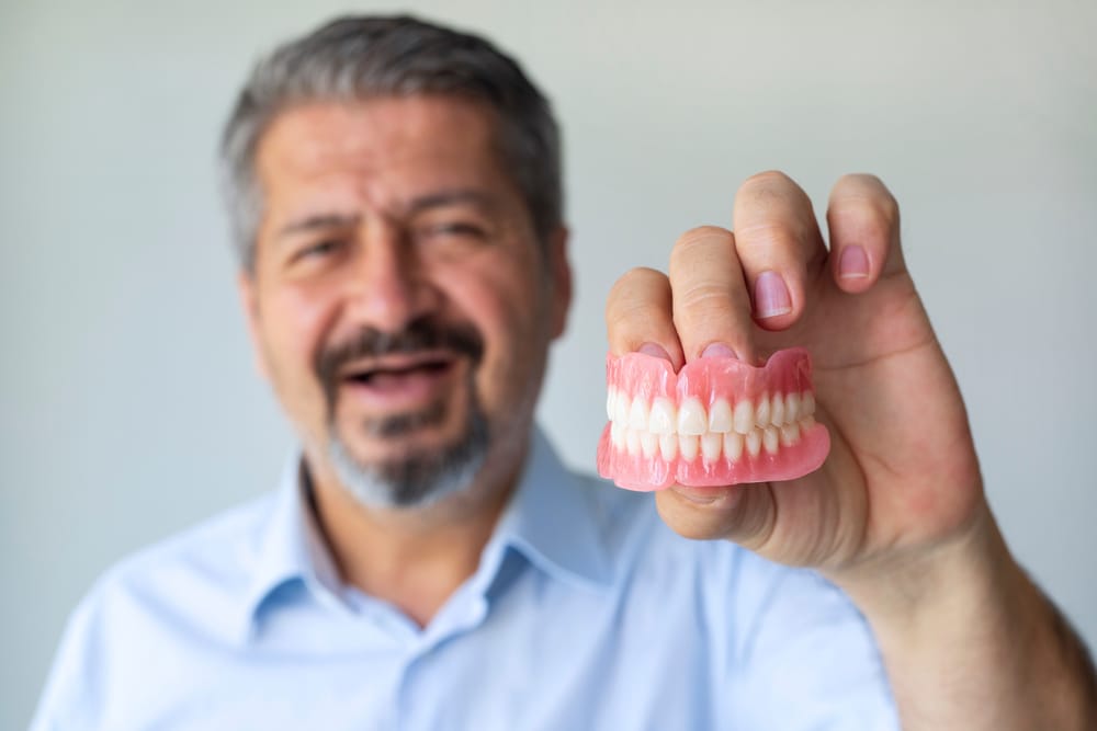 Middle-aged man holding dentures - Dentures in Seattle