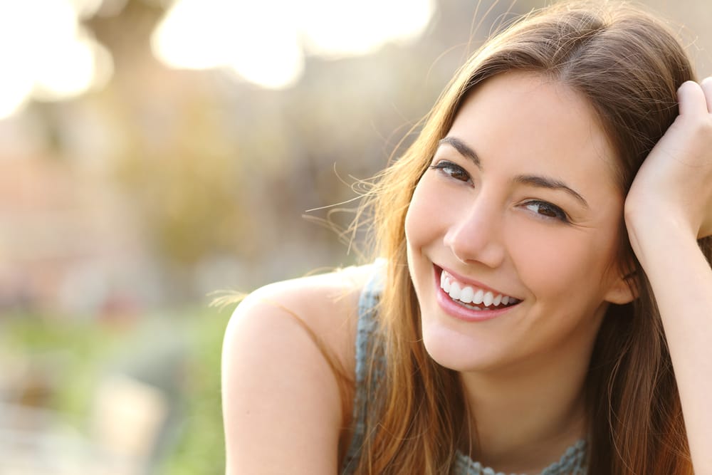 Woman smiling with perfect smile and white teeth in a park and looking at camera - Invisalign in Seattle