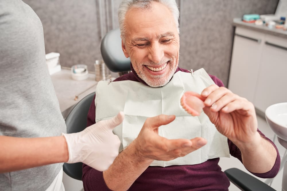 Elderly man holding dentures - Dentures in Seattle