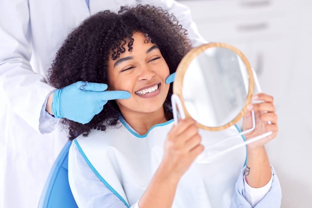 Woman holding a mirror looking at her teeth - Dental Implants in Seattle